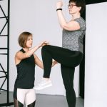 An elderly woman performs exercises with a fitness coach, focusing on a healthy lifestyle and wellness indoors.
