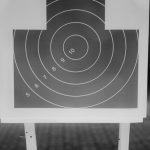 Black and white image of a shooting range target with numbered rings, highlighting aim precision.